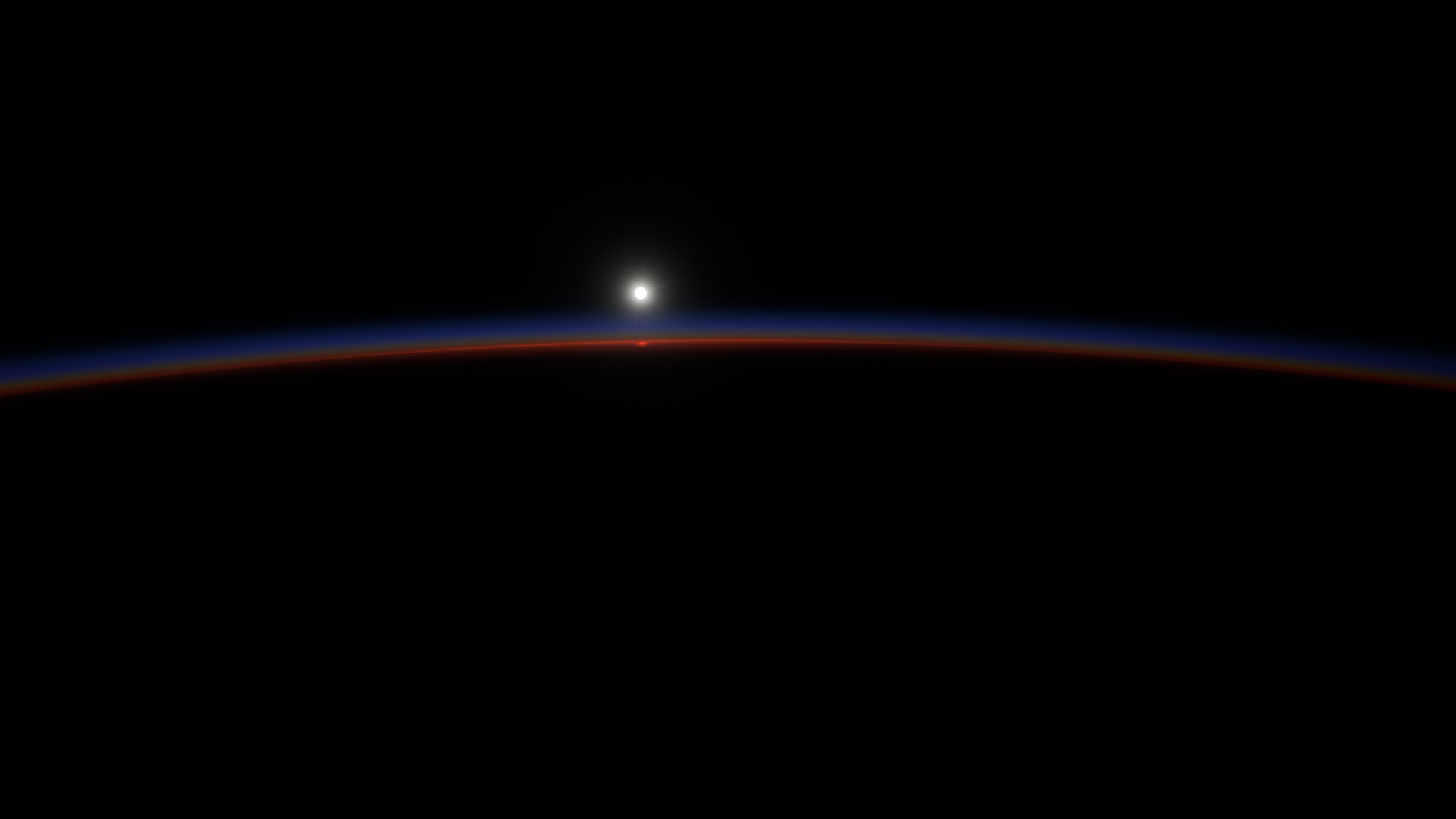 Sunrise from orbit: the Sun on the curved edge of the Earth, the thin band of the air glowing red and blue against black space.